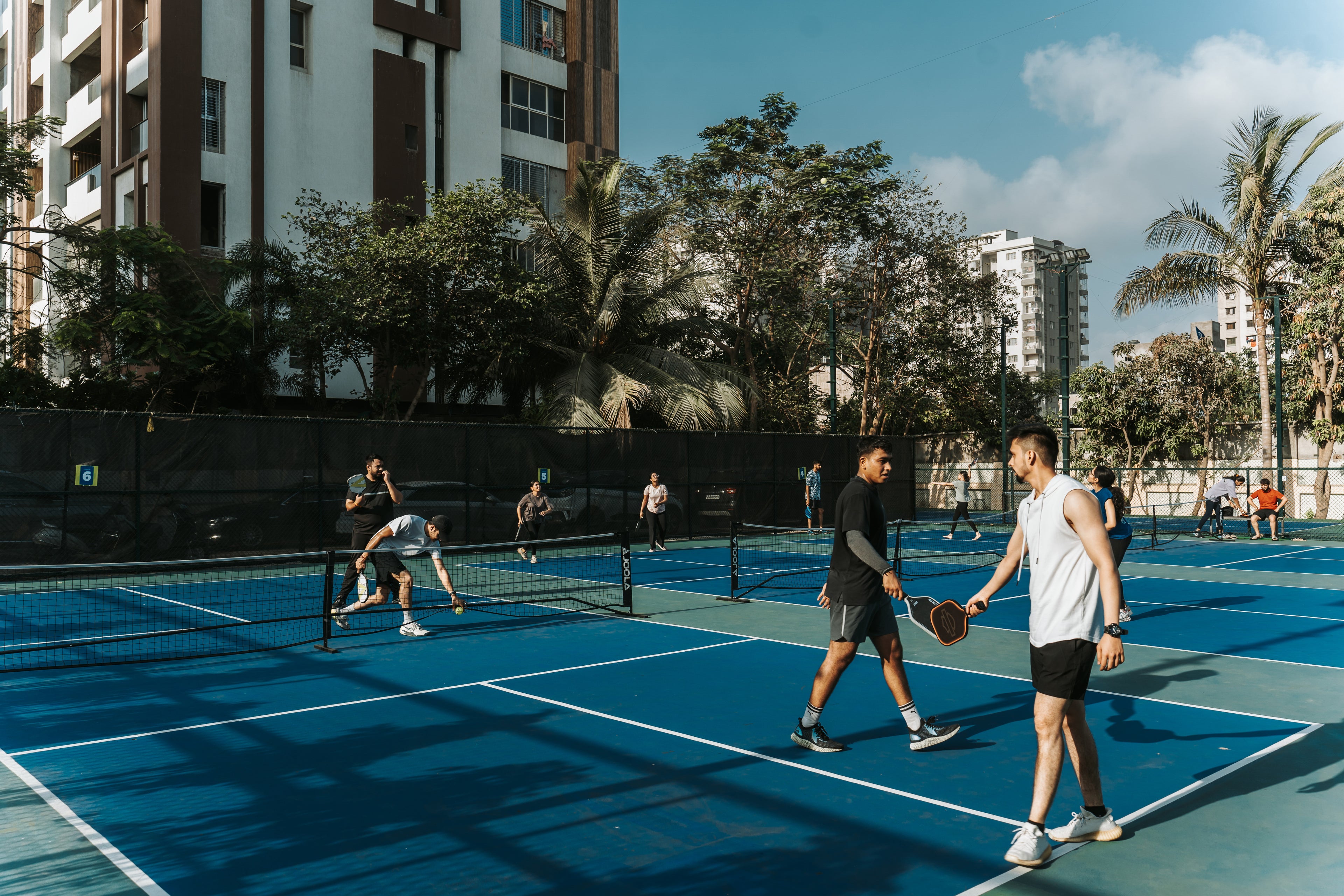 Velka's founder and his friends playing pickleball on an outdoor court with buildings and trees in the background